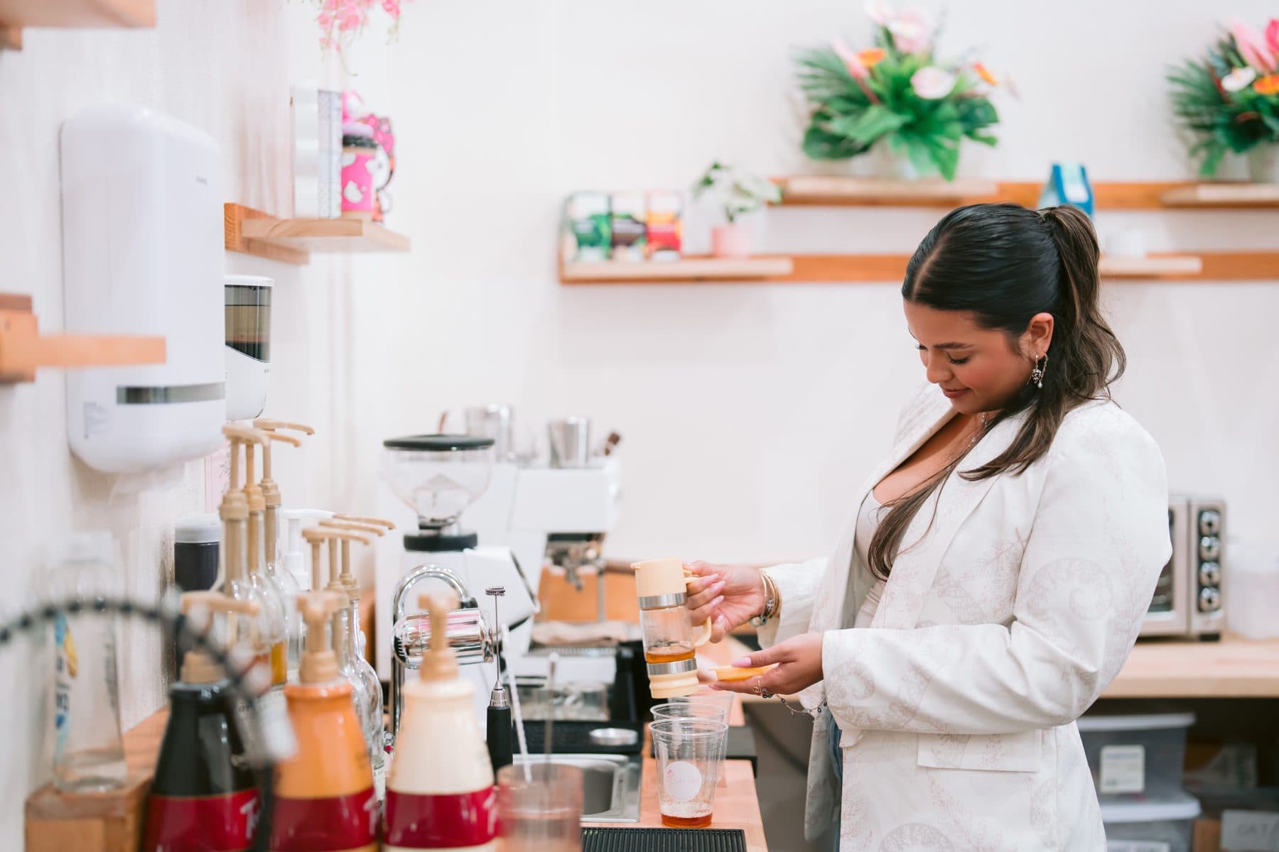 A Sip n' Pretty barista building a drink at the espresso bar, syrups and fresh florals lining the counter.