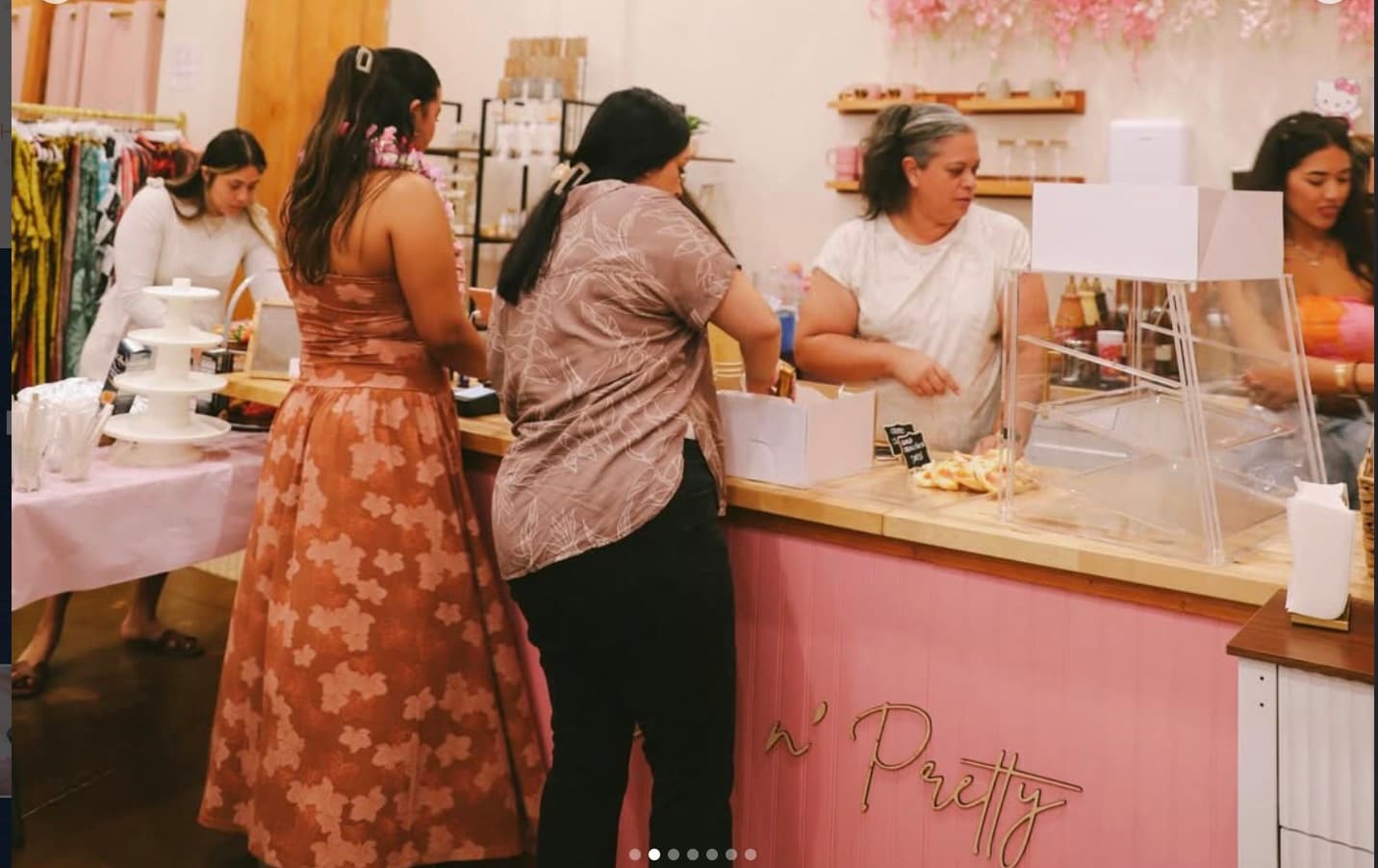 Inside Sip N' Pretty, customers at the pink scalloped counter, pink florals hanging above, baristas working.