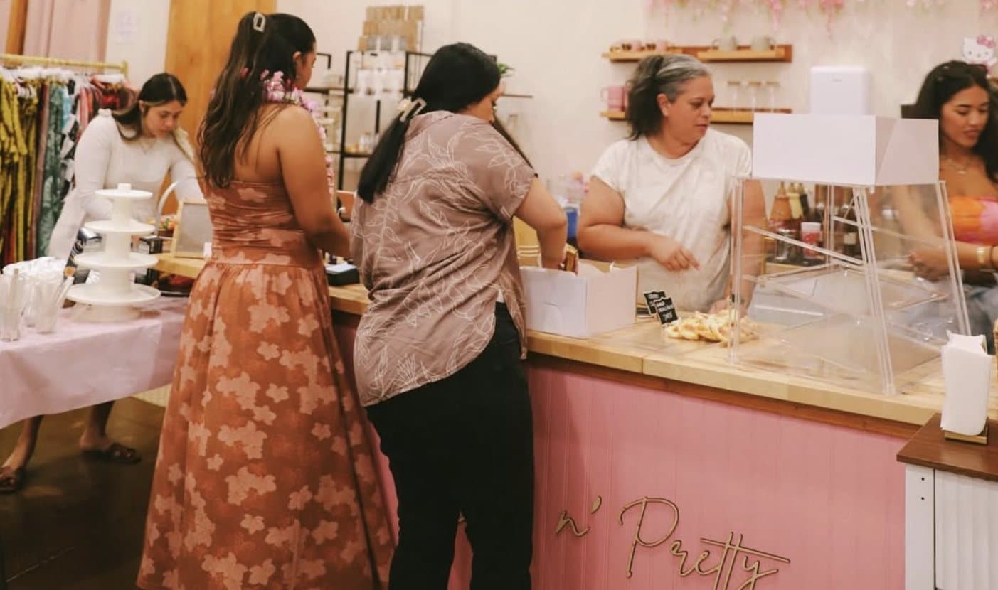 Inside Sip n' Pretty, customers at the pink scalloped counter, pink hanging florals, baristas working behind the bar.