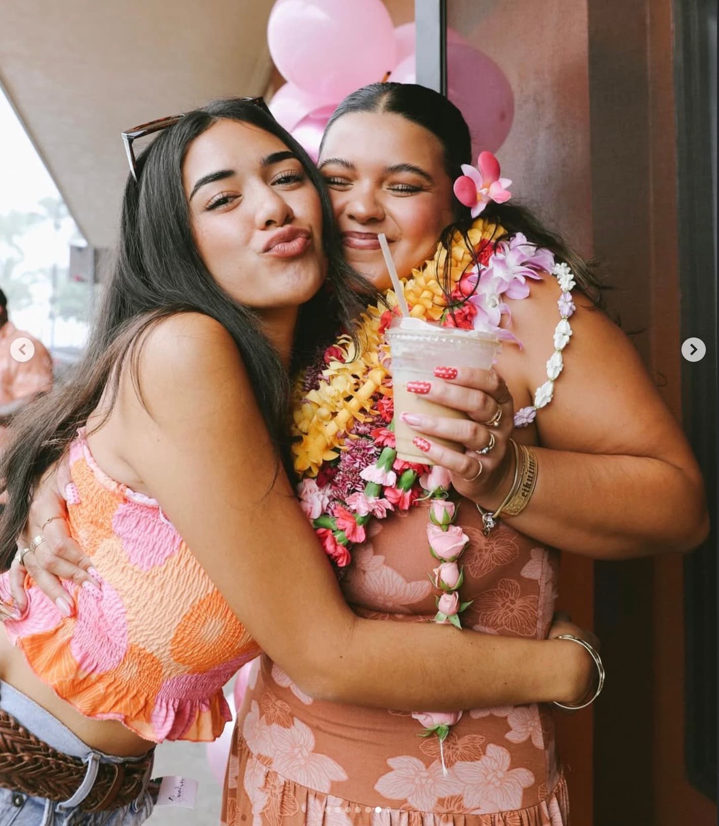Two friends embracing at Sip N' Pretty, one holding a tropical iced drink, wearing fresh leis.