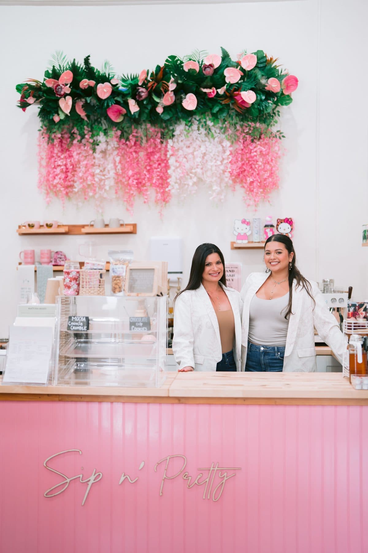 The mother-and-daughter team behind the pink Sip n' Pretty counter, espresso bar and fresh florals behind them.