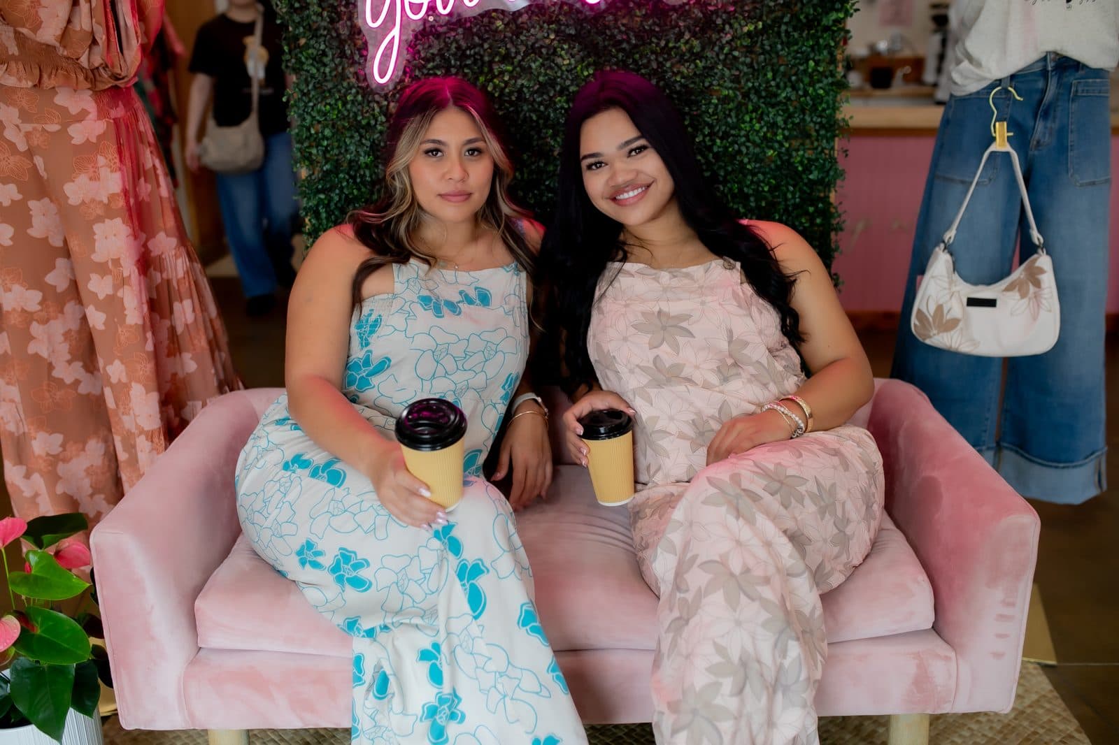 Two friends toasting iced Sip n' Pretty drinks at the counter on opening day, fresh leis.